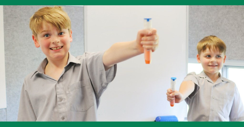 Two young boys in school uniforms holding epinephrine auto-injectors and smiling