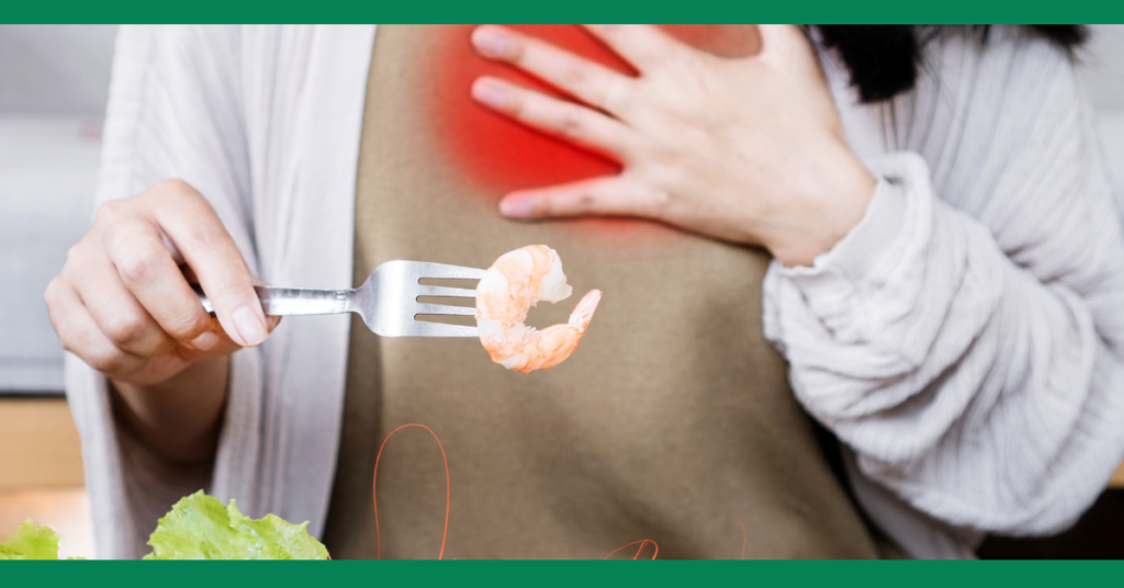 Person holding their chest in pain while holding a shrimp on a fork, indicating a possible allergic reaction.