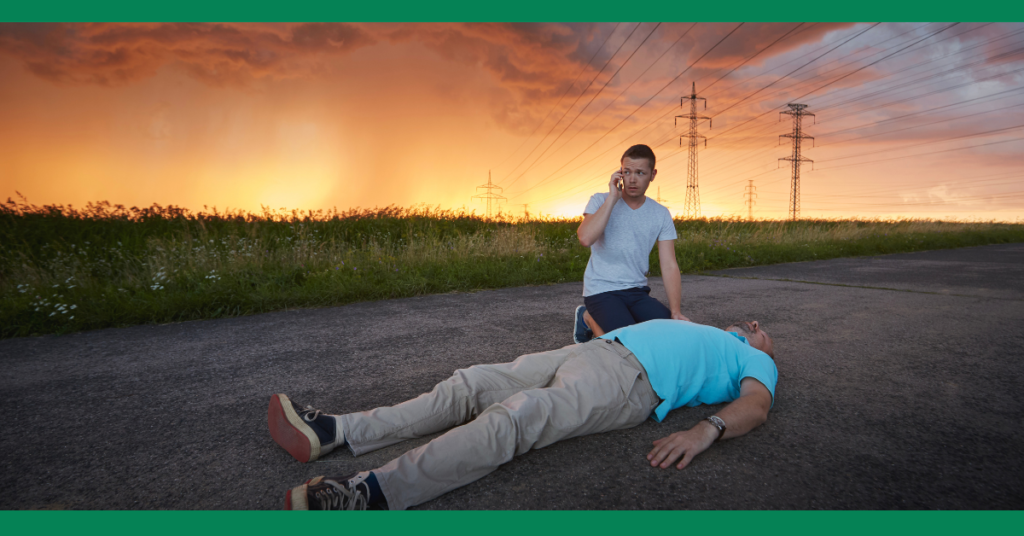 a man calls emergency services while someone unconscious lies on the road