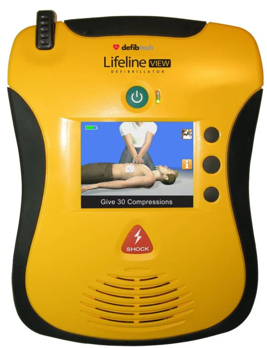 A yellow Lifeline VIEW defibrillator from Defibtech. The device features a screen displaying an instructional video showing a person performing chest compressions on a mannequin, with the instruction "Give 30 Compressions" visible. The defibrillator has a prominent red "SHOCK" button and several other control buttons on the right side.






