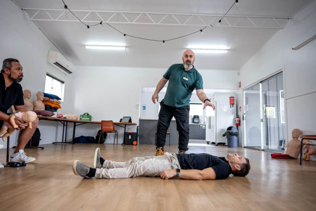 Step 1 of the recovery position: A first aid instructor begins the demonstration by preparing a person lying on the floor while another person observes